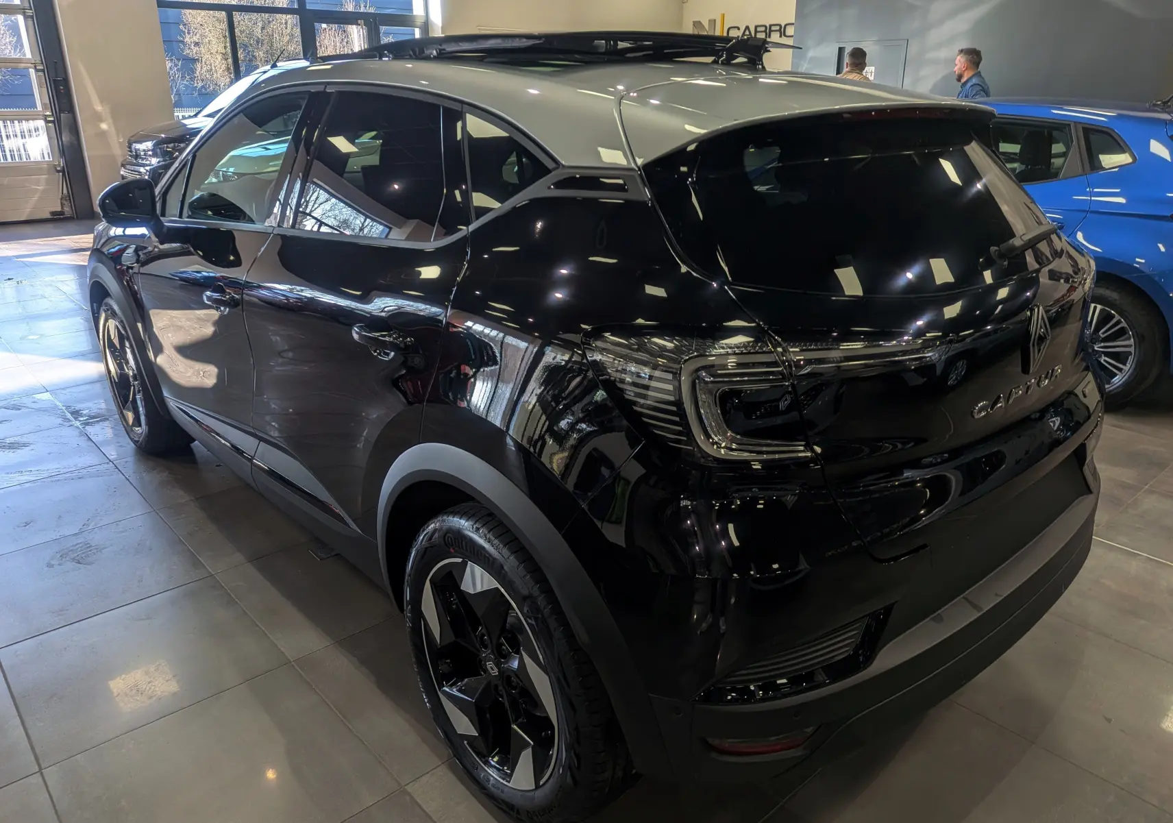 Vue 3/4 arrière droite du Renault Captur E-TECH noir avec toit gris Highland, en intérieur showroom, soulignant ses jantes bi-ton.