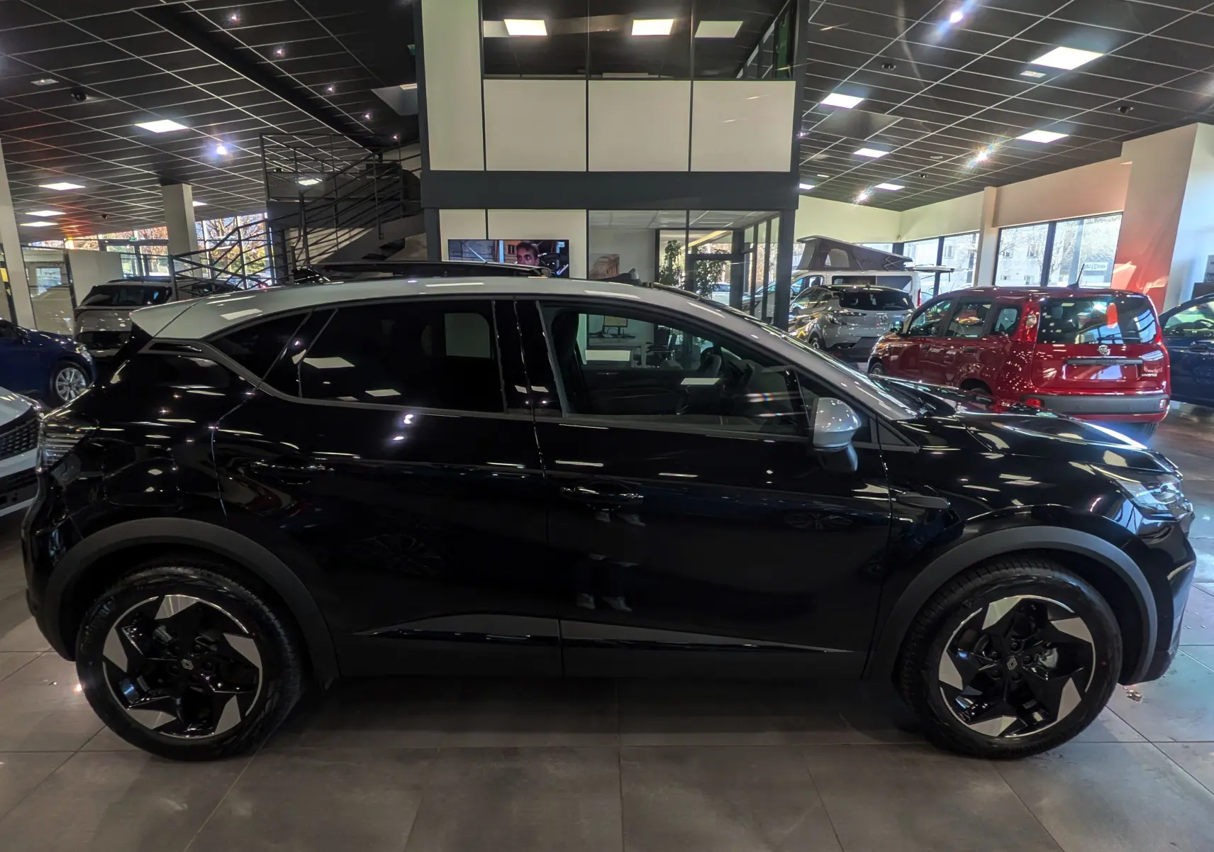 Profil côté gauche du Renault Captur E-TECH hybride noir avec toit gris Highland et jantes noires biton dans un showroom.