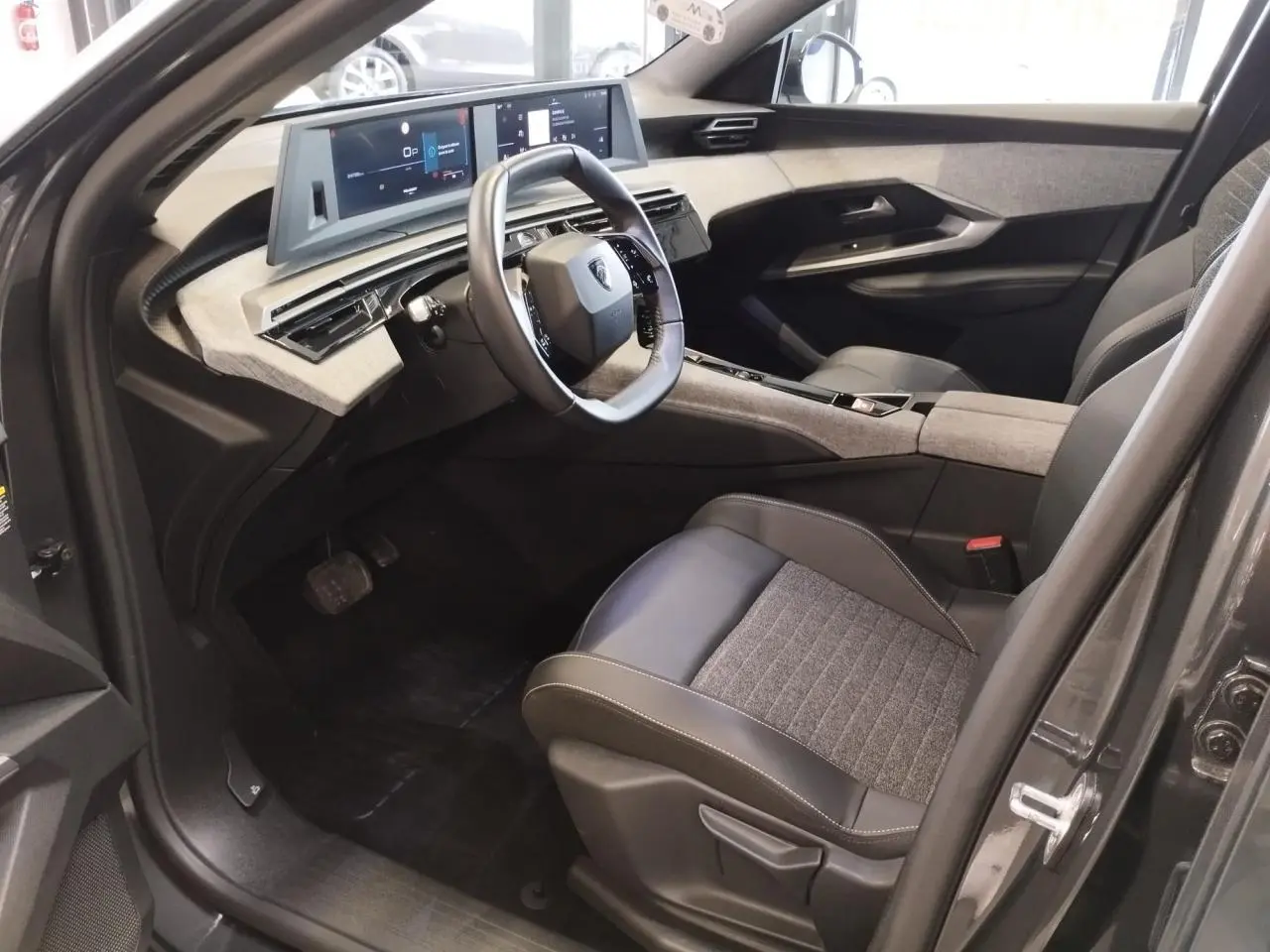 Intérieur avant droit du Peugeot 5008 gris titanium 2025 avec tableau de bord numérique et sellerie tissu cuir.
