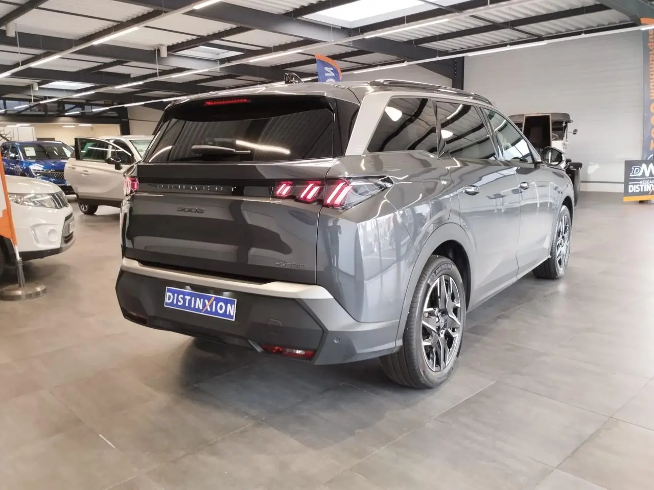 Vue 3/4 arrière droite d'un Peugeot 5008 gris titanium avec feux arrière LED 3 griffes en showroom.