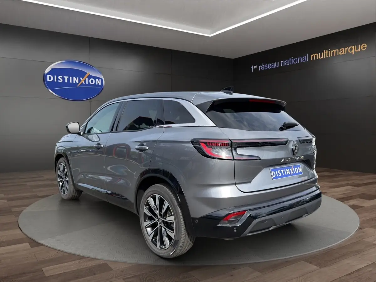 Vue 3/4 arrière droite du Renault Austral Techno E-Tech gris foncé avec feux LED et toit spoiler en intérieur showroom.