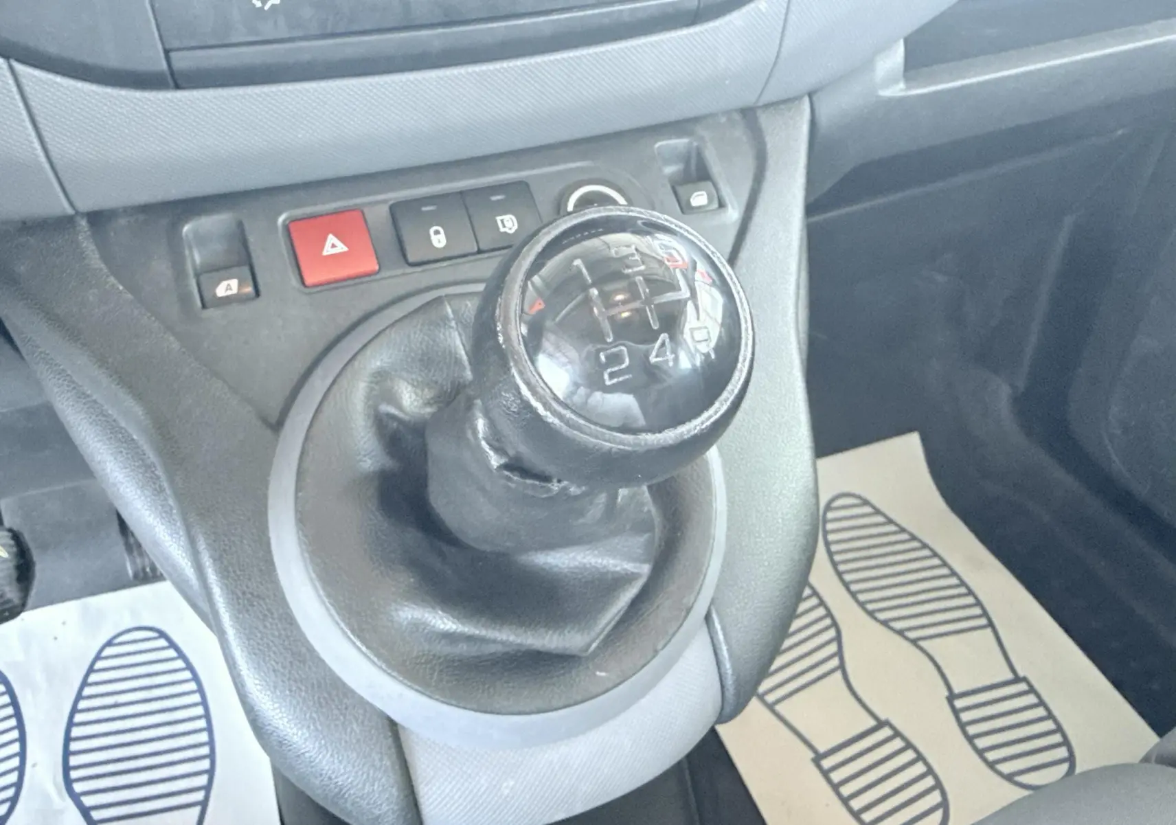 Gros plan sur le levier de vitesses manuel noir du Peugeot Partner blanc, avec boutons de commande et tapis de sol visibles.