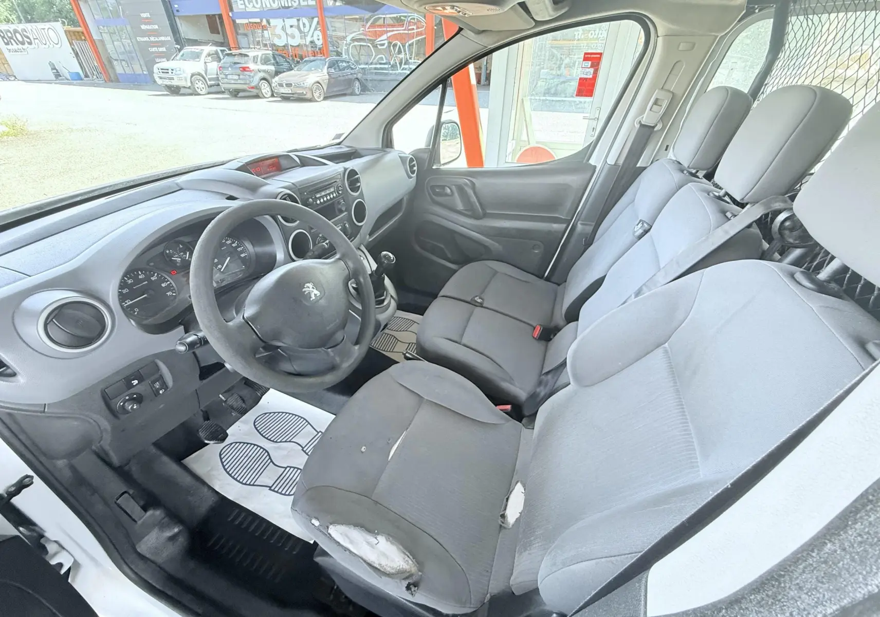 Vue intérieure côté conducteur du Peugeot Partner blanc 2014, montrant le volant, la boîte manuelle et les sièges usés.