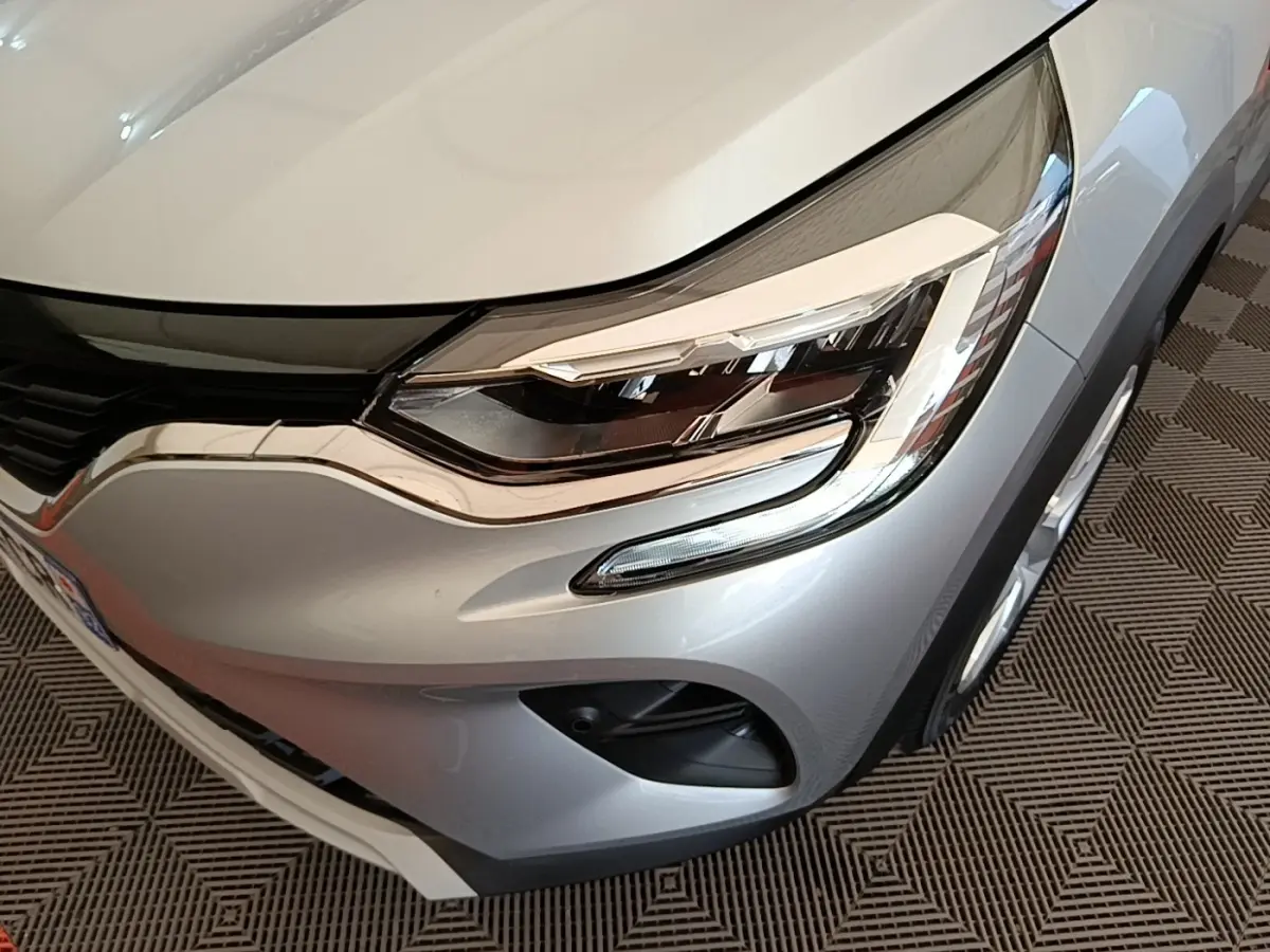 Gros plan sur l'avant droit gris clair du Renault Captur Business E-Tech hybride 2022, mettant en valeur le phare LED et la calandre.