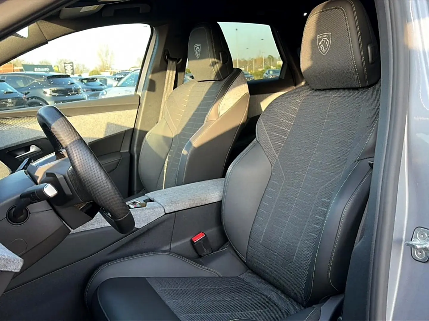 Intérieur Peugeot 3008 gris, vue côté conducteur montrant sièges sport avec logo Peugeot brodé sur les appuis-tête.