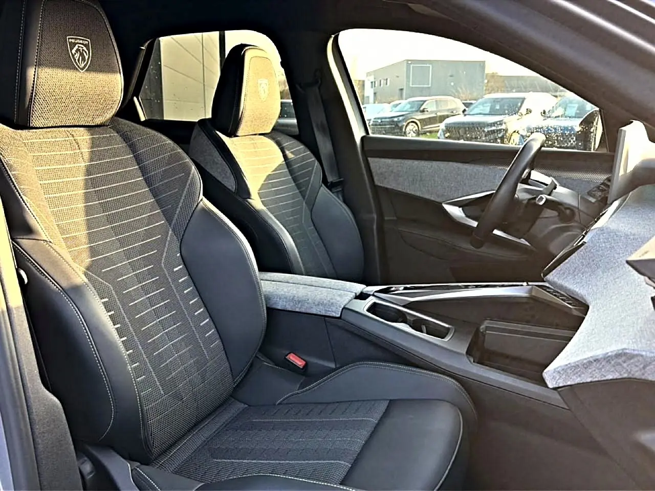 Vue intérieure côté conducteur du Peugeot 3008 gris 2025, sièges en tissu et cuir avec logo Peugeot brodé.