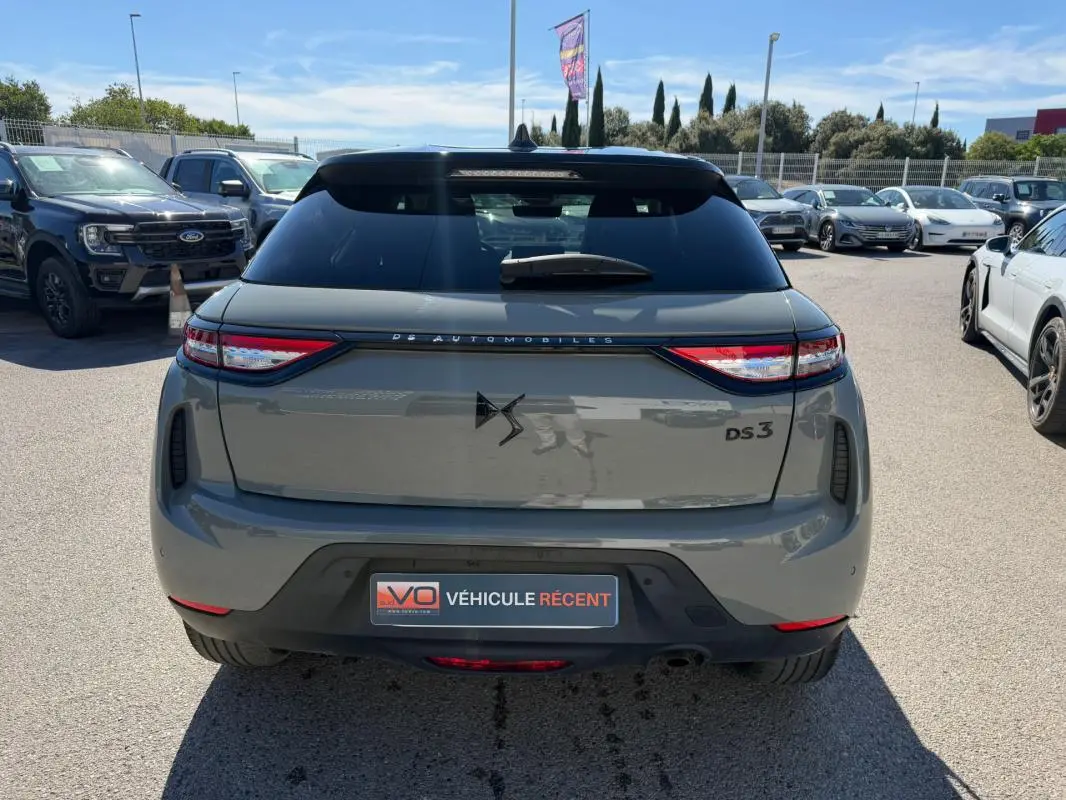 Vue arrière d'une DS3 gris 2024 avec logo DS et feux arrière fins, stationnée en extérieur sur un parking.