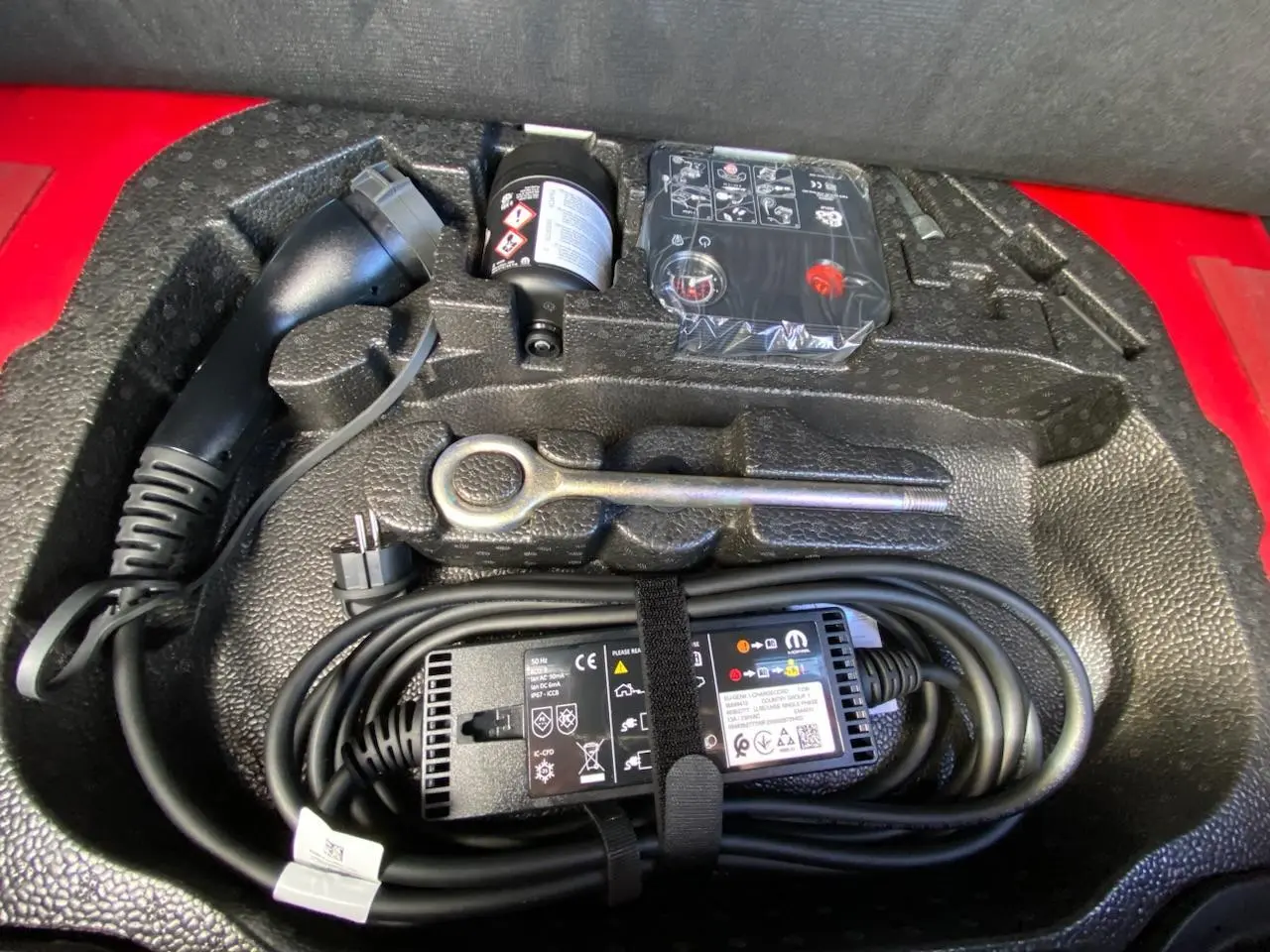 Gros plan sur le compartiment de rangement rouge du FIAT 500 Cabriolet Electrique avec câble de recharge et outils.