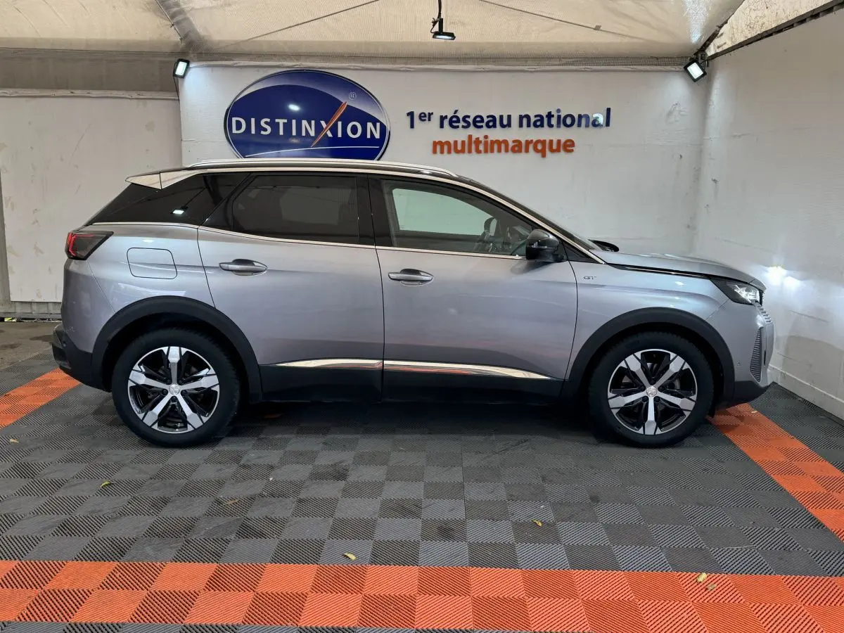 Profil droit d’un Peugeot 3008 GT gris clair 2021, avec jantes alliage et toit noir dans un garage.