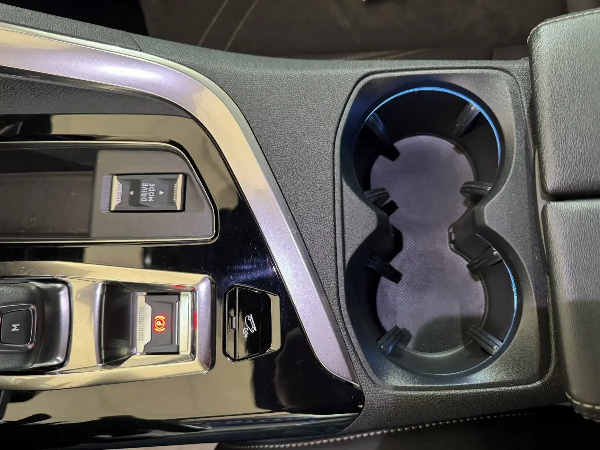 Gros plan sur la console centrale noire brillante du Peugeot 3008 gris clair, avec porte-gobelets et commandes électroniques.