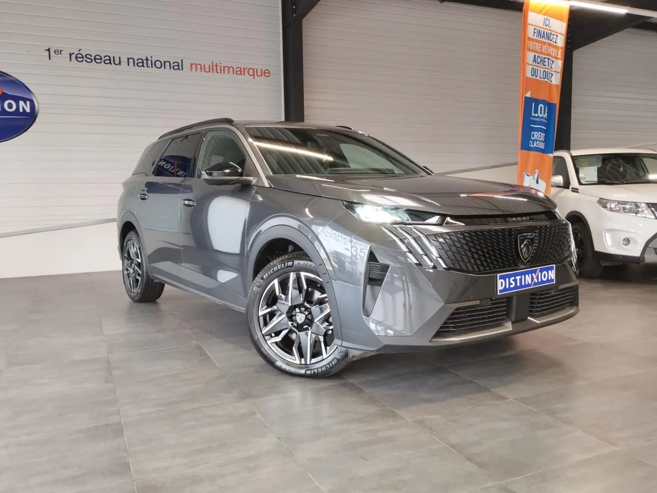 Peugeot 5008 gris titanium en 3/4 avant droit, avec calandre noire et jantes alliage 19'' diamantées.