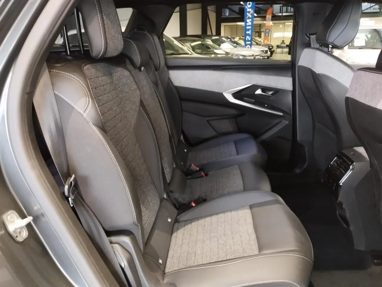 Vue latérale des sièges arrière en tissu gris et cuir sur Peugeot 5008 gris titanium, avec porte et console centrale visibles.