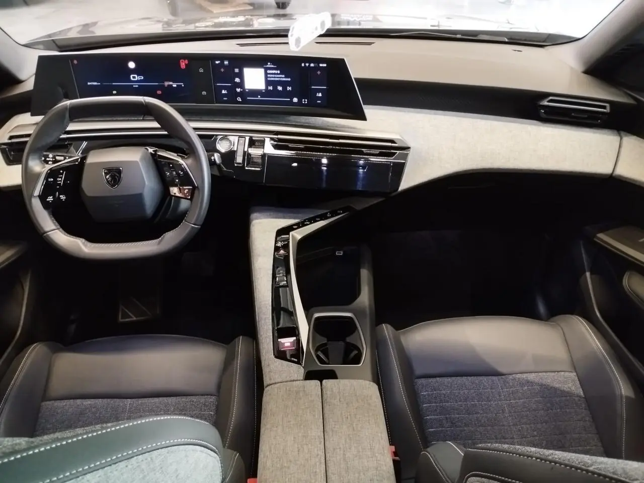 Vue intérieure avant du Peugeot 5008 2025, tableau de bord et volant noir avec inserts tissu gris clair.
