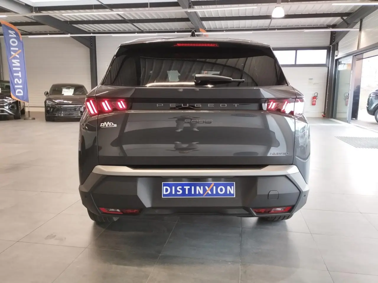 Vue arrière d’un Peugeot 5008 gris titanium avec feux arrière LED 3 griffes allumés en showroom.