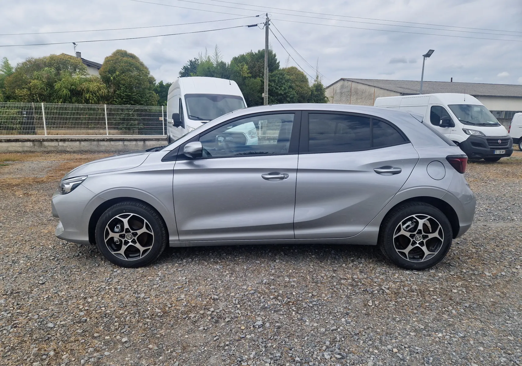 Vue de profil côté gauche d'une MG3 1.5L Hybrid+ 195CH Luxury en finition Cosmic Silver Metal sur un sol gravillonné.