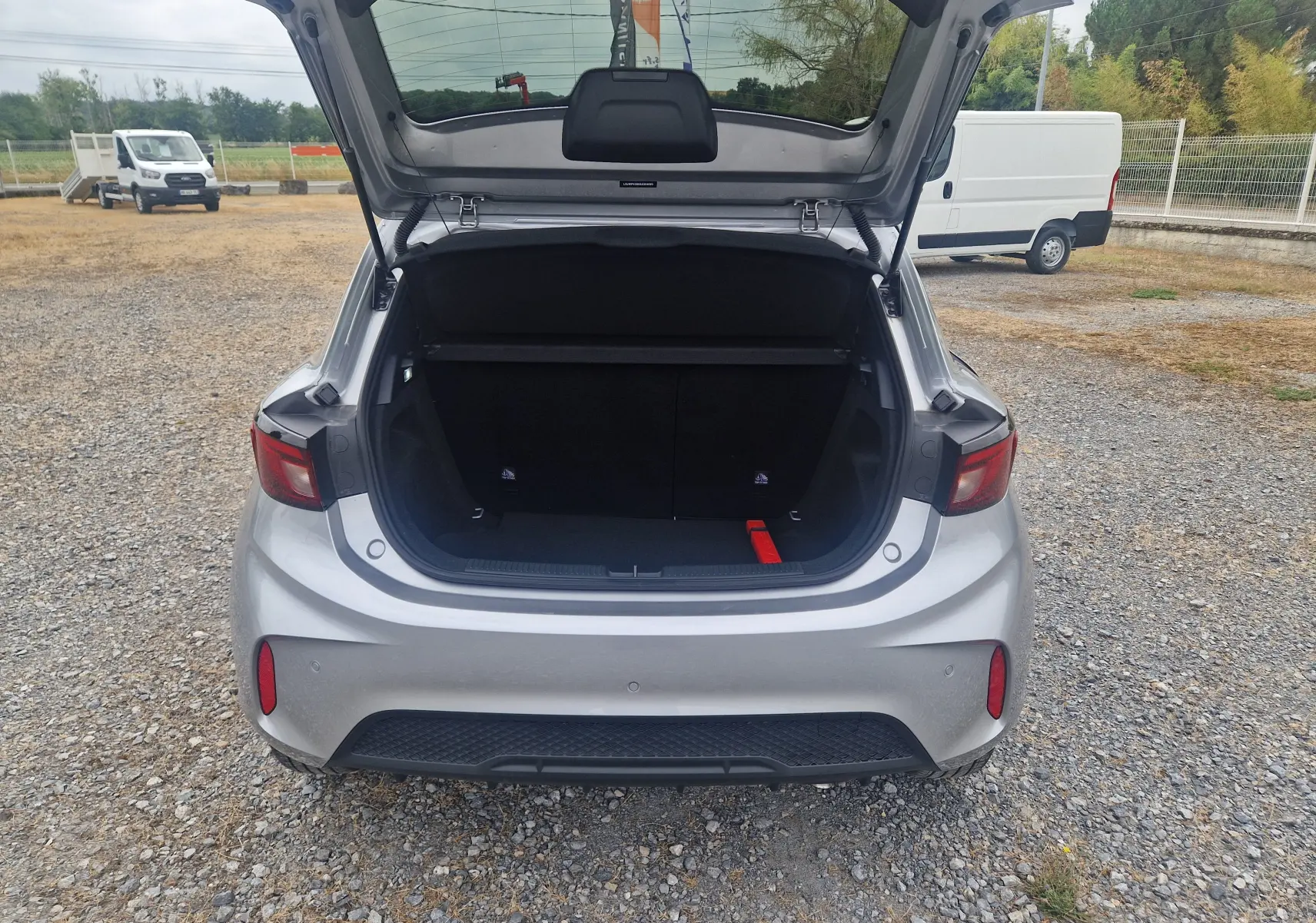 Vue arrière du coffre ouvert de la MG3 1.5L Hybrid+ 195ch Luxury en Cosmic Silver Metal sur sol gravillonné.