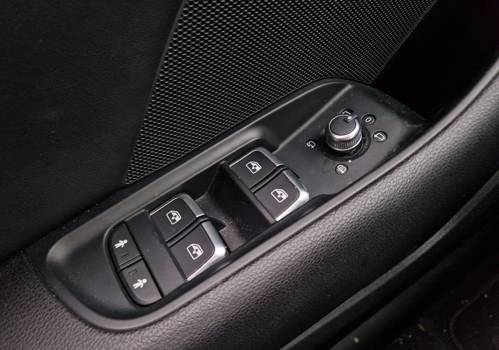 Gros plan sur les commandes de lève-vitres et réglage des rétroviseurs côté conducteur d’une Audi A3 Sportback noire.