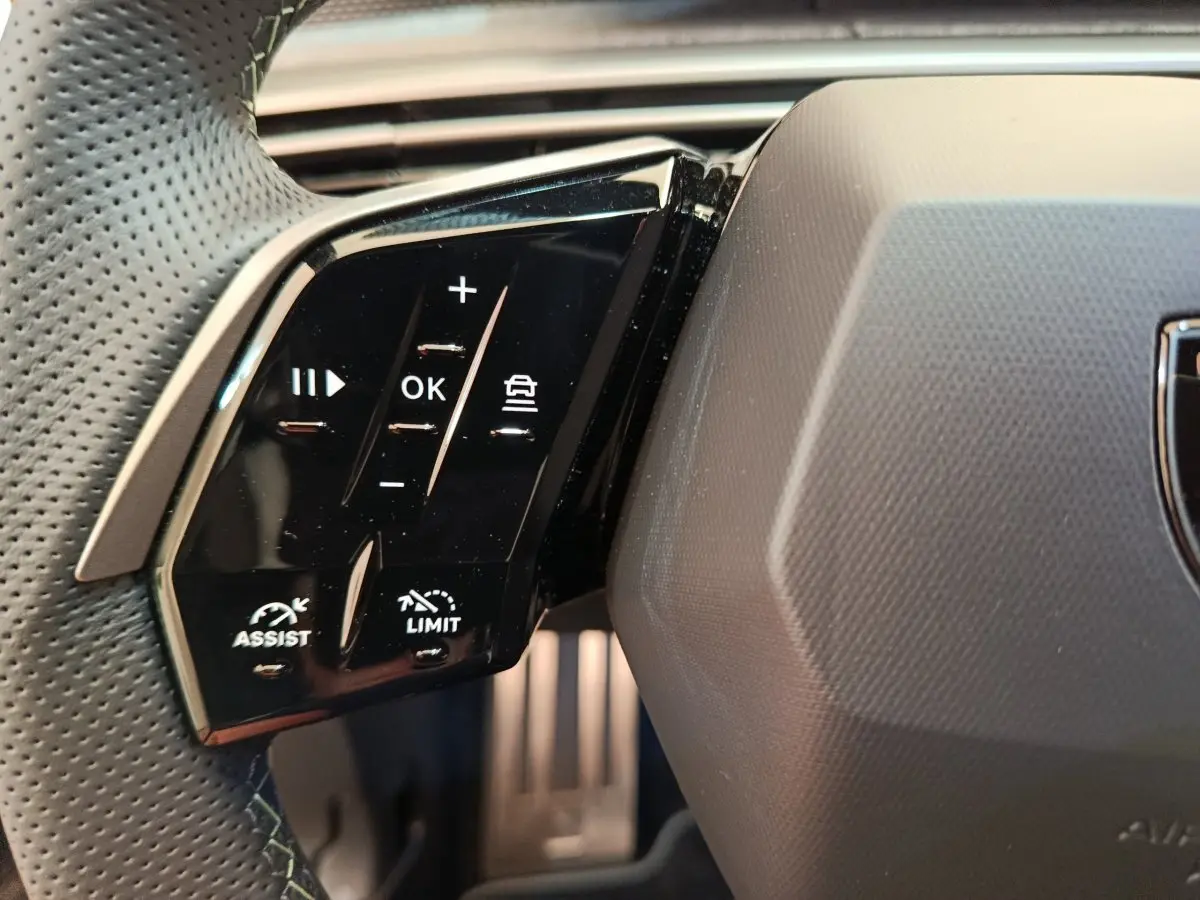 Gros plan sur les commandes gauche du volant cuir perforé du Peugeot 3008 1.2 Hybrid 145 GT noir, avec boutons multifonctions.