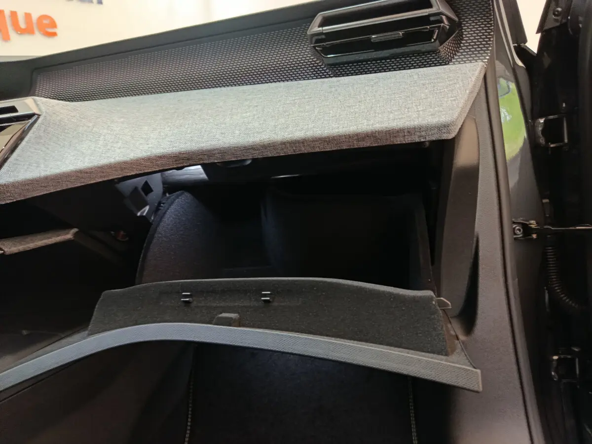 Intérieur du Peugeot 3008 2025 noir, vue sur la boîte à gants ouverte avec tableau de bord gris clair texturé.