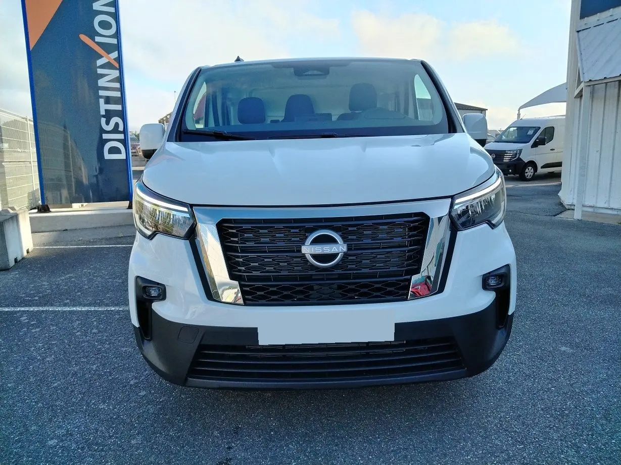 Vue de face d'un Nissan Primastar blanc 2025 avec calandre noire et détails chromés sur un parking extérieur.