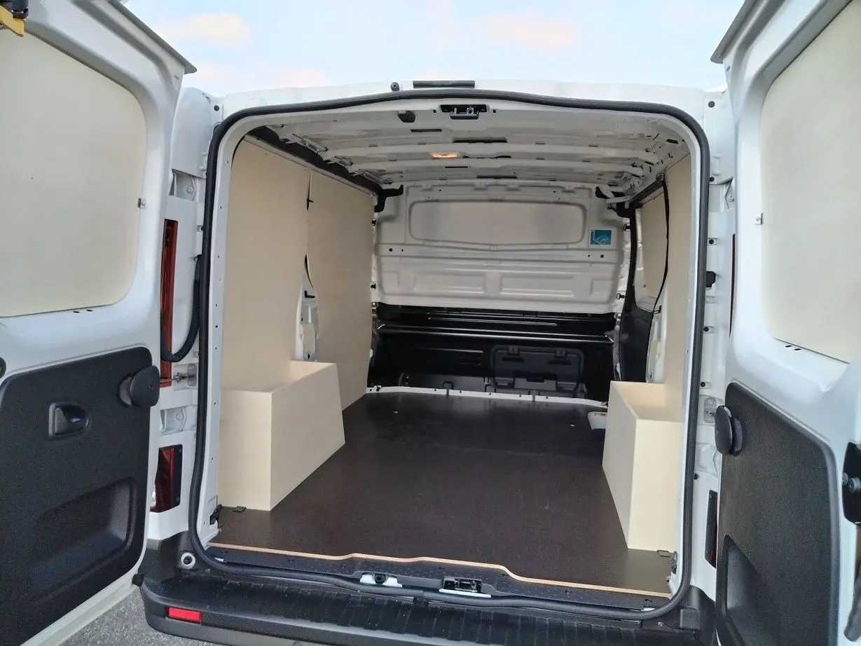 Vue arrière ouverte du Nissan Primastar blanc 2025 avec aménagement bois intérieur et plancher noir.