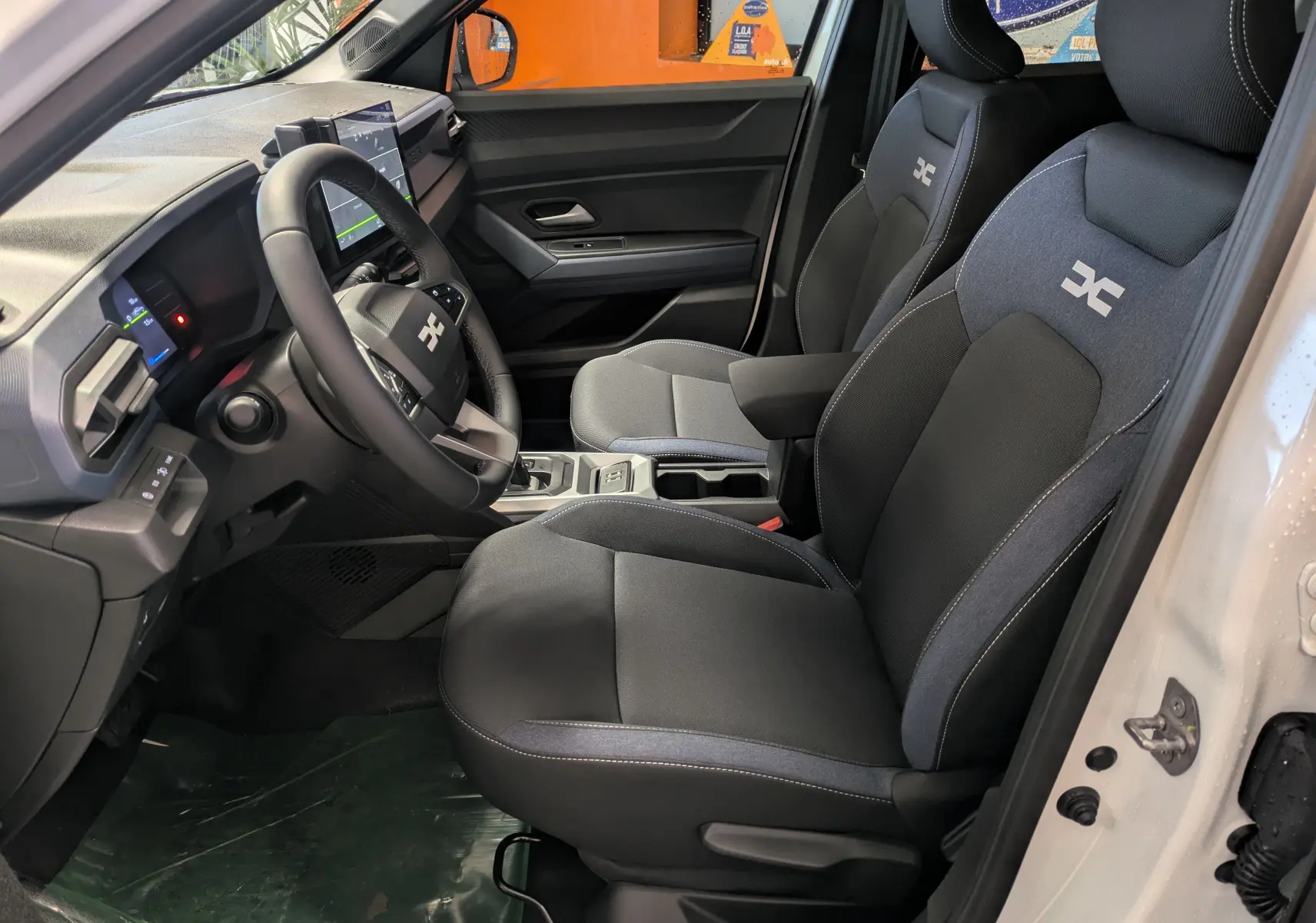 Vue intérieure côté gauche du Dacia Duster Hybrid 140 Journey blanc glacier, mettant en valeur les sièges avant et le tableau de bord moderne.