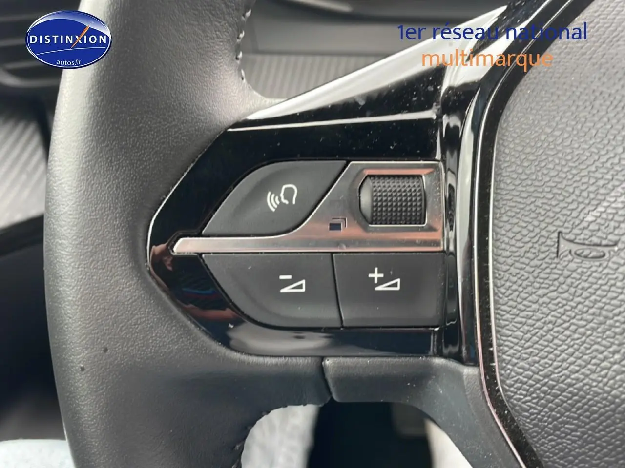 Gros plan sur les commandes gauche du volant noir du Peugeot 2008 E-136 allure gris sélénite, boutons de volume et appel mains-libres.