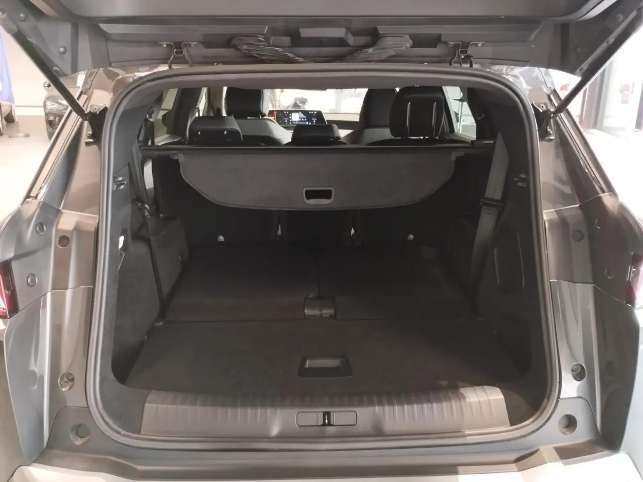 Coffre ouvert vu de l'arrière d'un Peugeot 5008 gris titanium, banquette arrière rabattue et cache-bagages déployé.