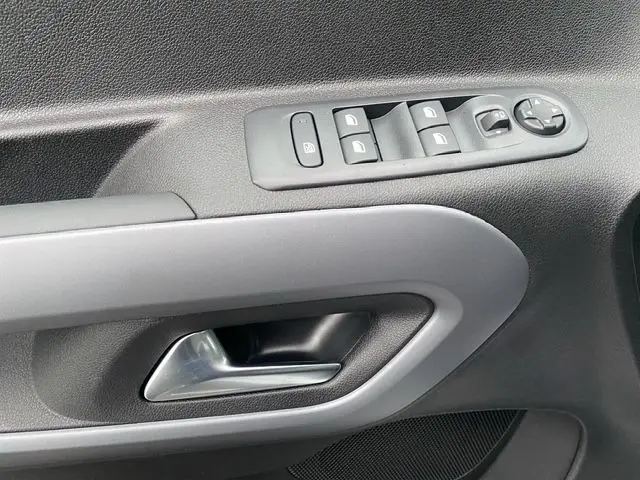 Gros plan sur la poignée intérieure et les commandes électriques de la porte côté conducteur du Citroën Berlingo blanc.