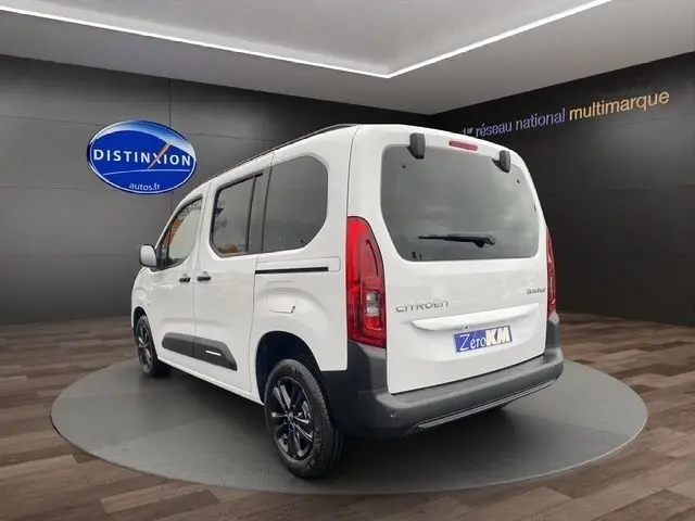 Vue 3/4 arrière droite d'un Citroën Berlingo blanc 2025 avec vitres teintées et jantes noires en showroom.