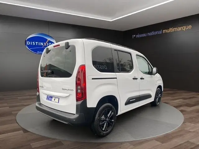 Vue 3/4 arrière droite d’un Citroën Berlingo blanc 2025 avec vitres teintées et jantes noires en showroom.
