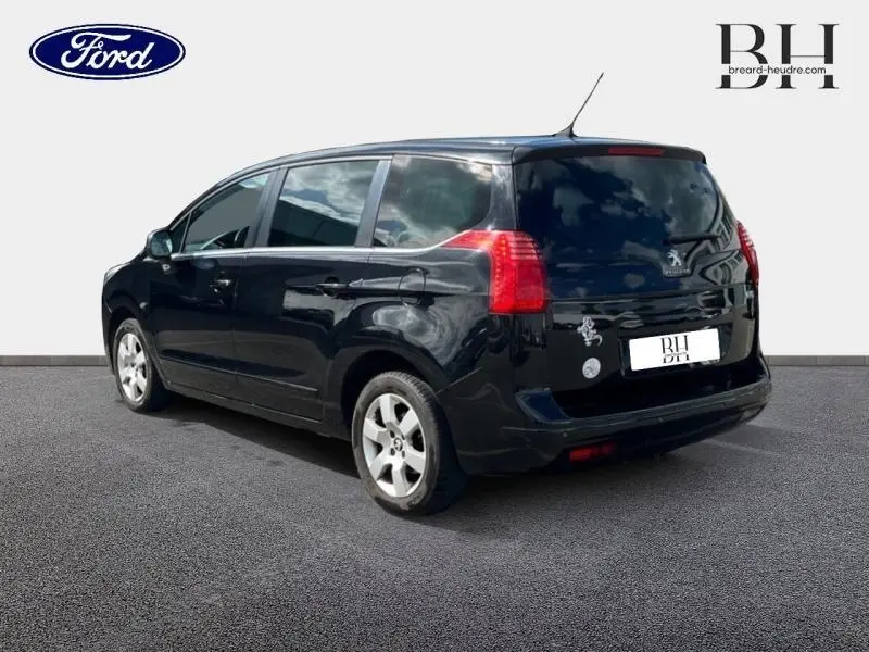 Vue 3/4 arrière droite d'un Peugeot 5008 noir Perla Nera avec vitres arrière surteintées et jantes alu.