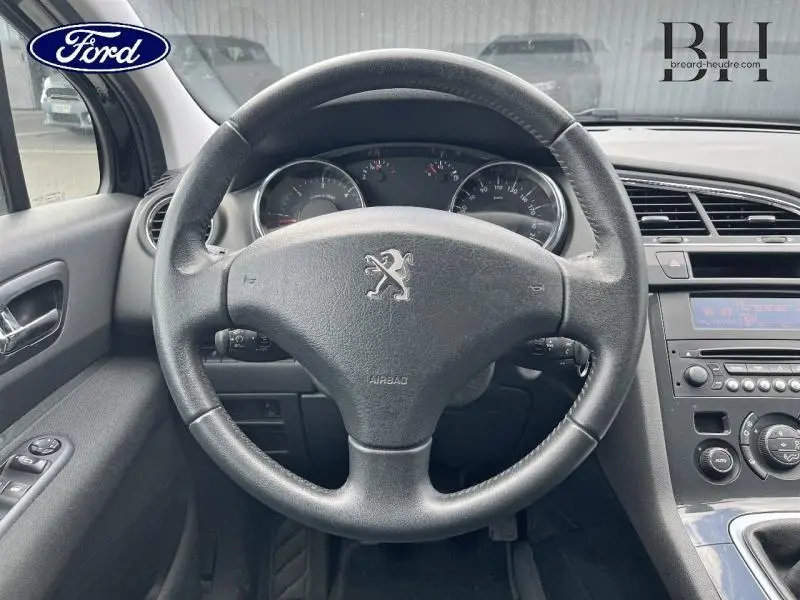 Vue intérieure centrée sur le volant noir de la Peugeot 5008 2015, avec tableau de bord et console centrale visibles.