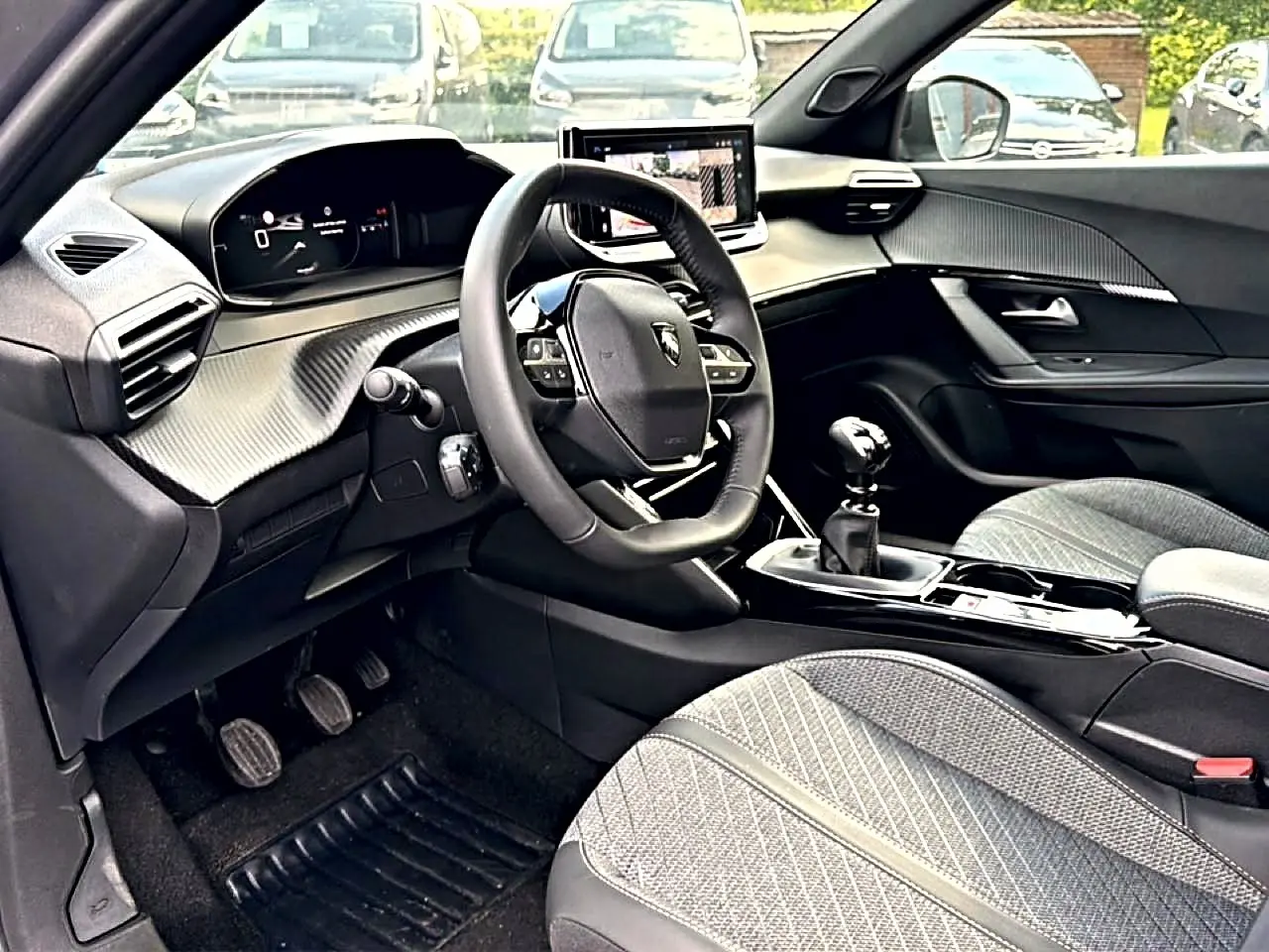 Intérieur avant droit du Peugeot 2008 1.2 100 Allure 2025, volant multifonction, boîte manuelle et sièges tissu gris.