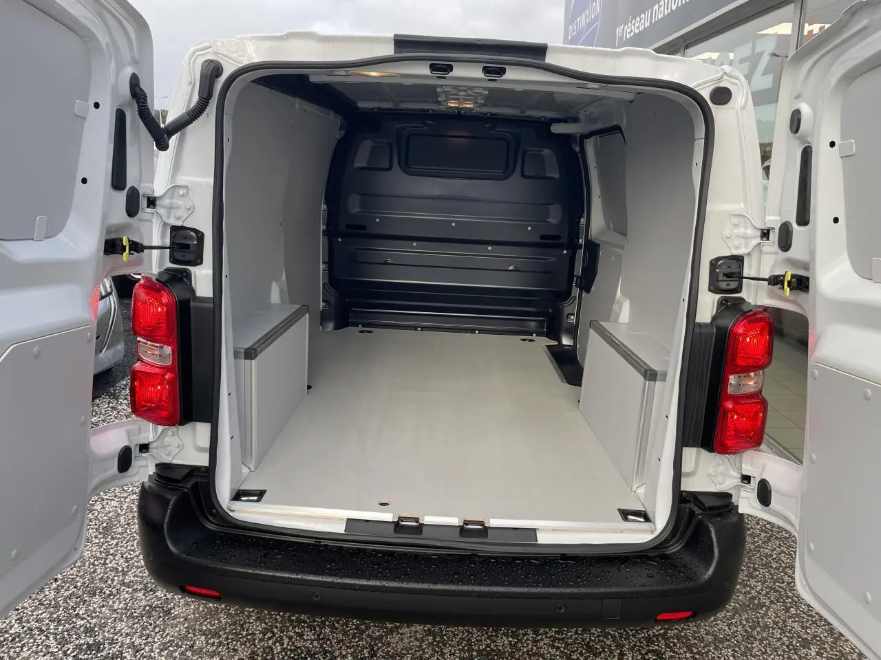 Vue arrière du fourgon blanc Opel Vivaro 2024 avec portes ouvertes montrant un plancher et coffrage en bois.
