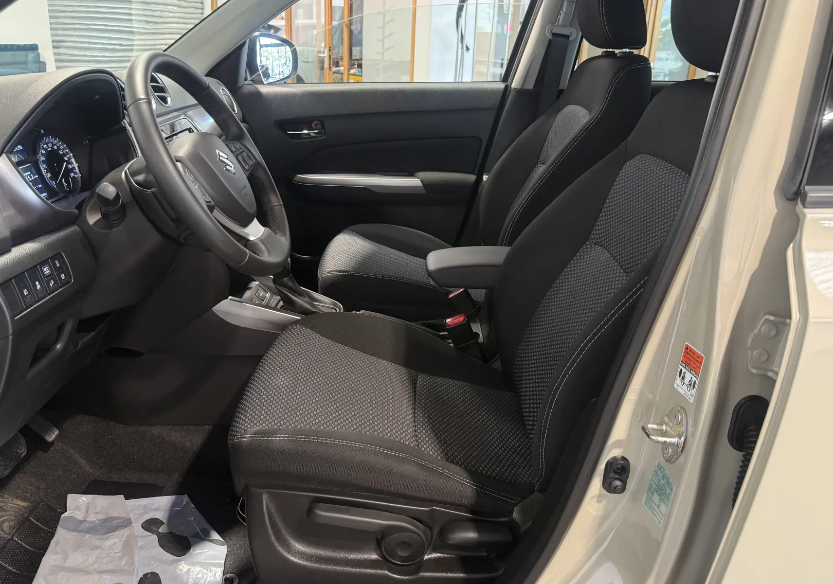 Intérieur côté conducteur du Suzuki Vitara beige 2023, montrant les sièges noirs et le tableau de bord avec volant multifonction.