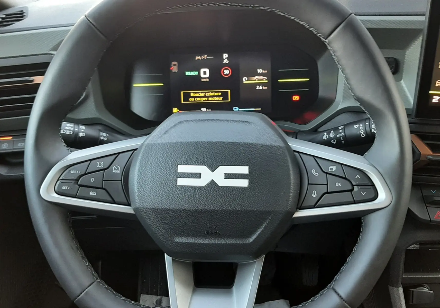 Volant noir avec logo DACIA stylisé, tableau de bord numérique et commandes intégrées, intérieur du Dacia Duster 2025.