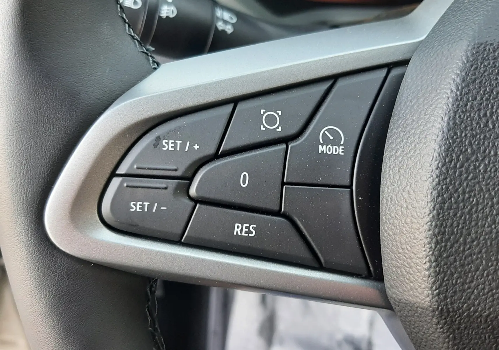 Gros plan sur les commandes au volant côté gauche du Dacia Duster 2025, boutons noirs avec cadre gris.