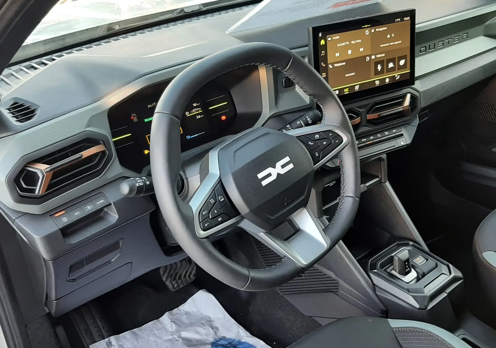 Vue intérieure du tableau de bord du Dacia Duster 2025 avec volant multifonction et écran tactile central.