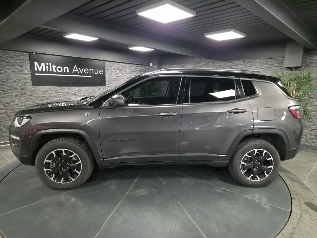 Profil côté gauche d'un Jeep Compass gris foncé avec jantes alliage noires et toit noir en showroom.