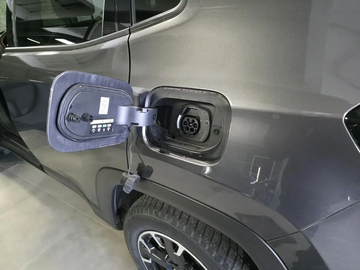 Prise de recharge ouverte côté gauche sur Jeep Compass gris foncé hybride rechargeable, avec jante alliage visible.