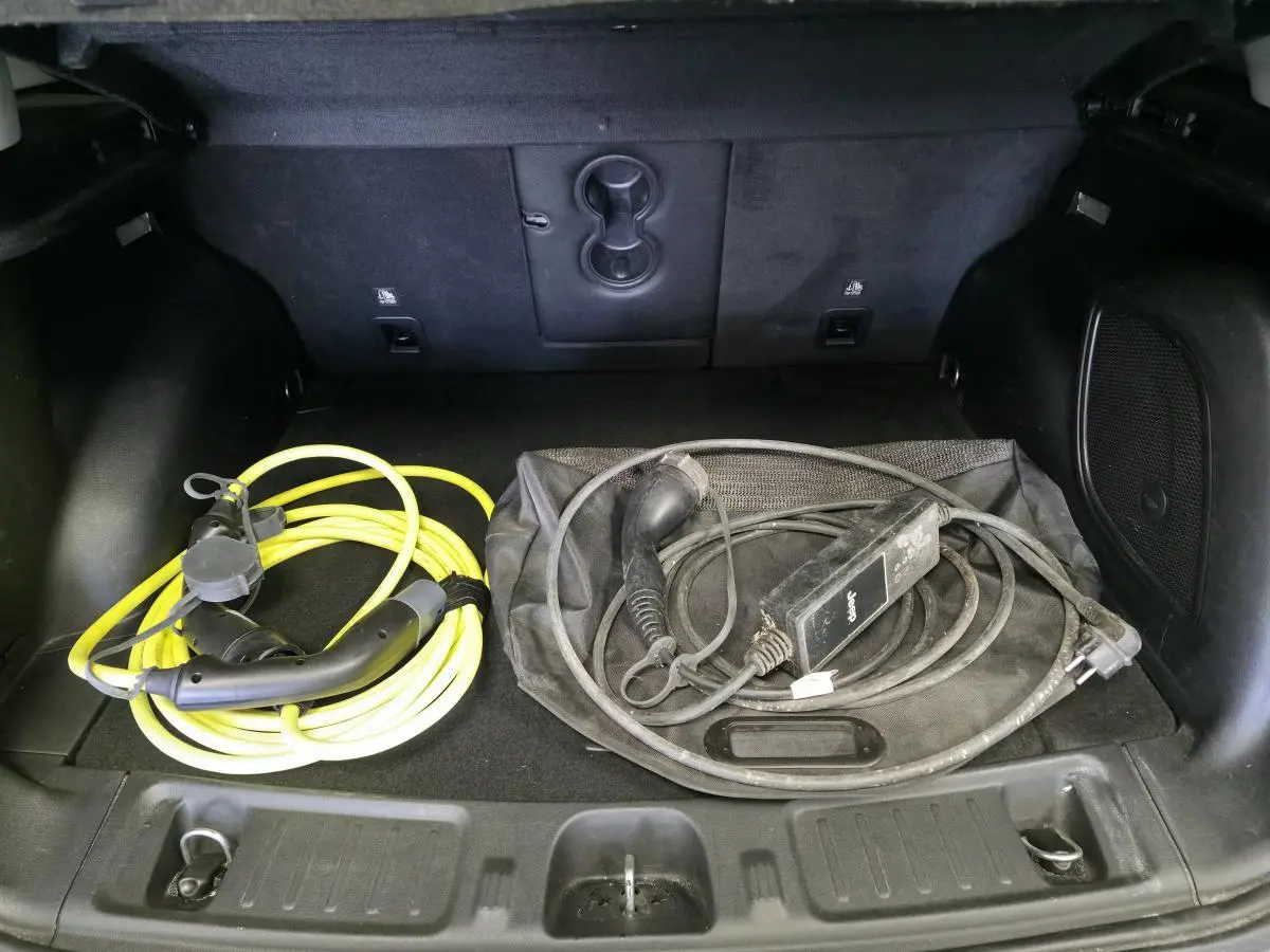 Coffre ouvert d’un Jeep Compass gris foncé montrant câbles de recharge hybride rangés sur le tapis noir.