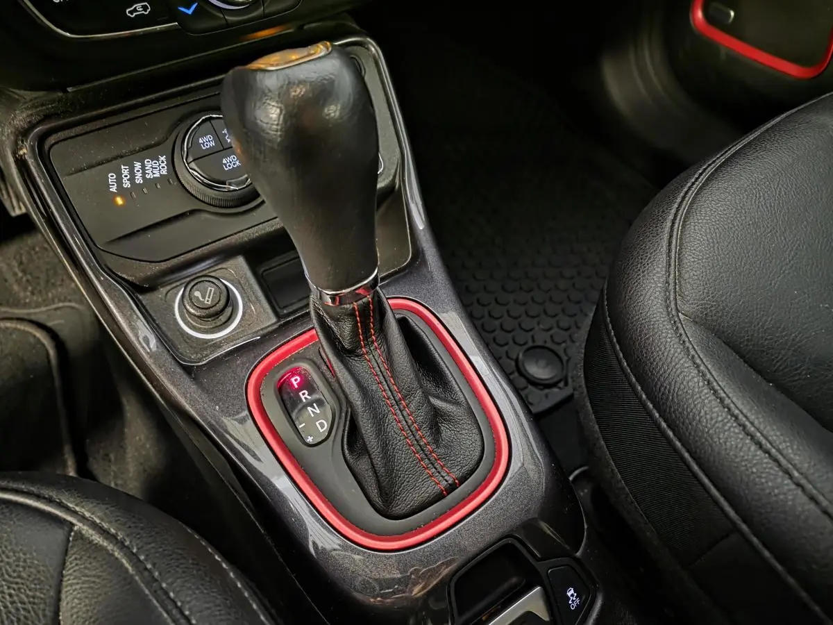 Gros plan sur la console centrale du Jeep Compass 2020 avec levier de vitesses cuir noir et surpiqûres rouges.