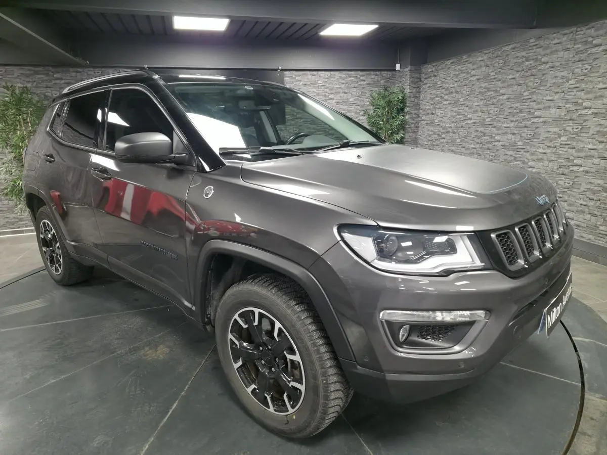 Jeep Compass gris foncé en vue 3/4 avant droit, avec jantes alliage noires et toit noir en intérieur showroom.