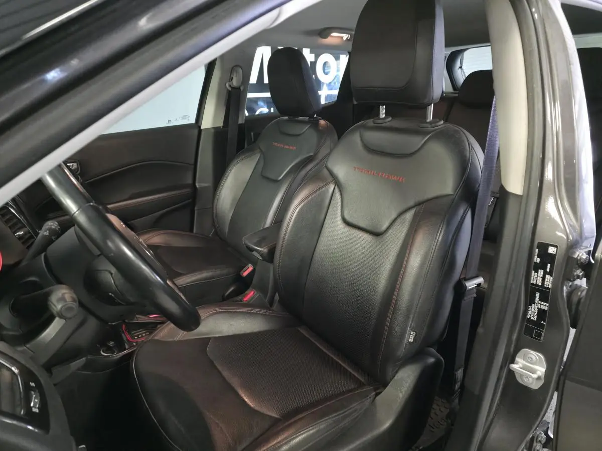 Vue intérieure côté conducteur du Jeep Compass gris foncé, sièges cuir noirs avec logo Trailhawk rouge brodé.