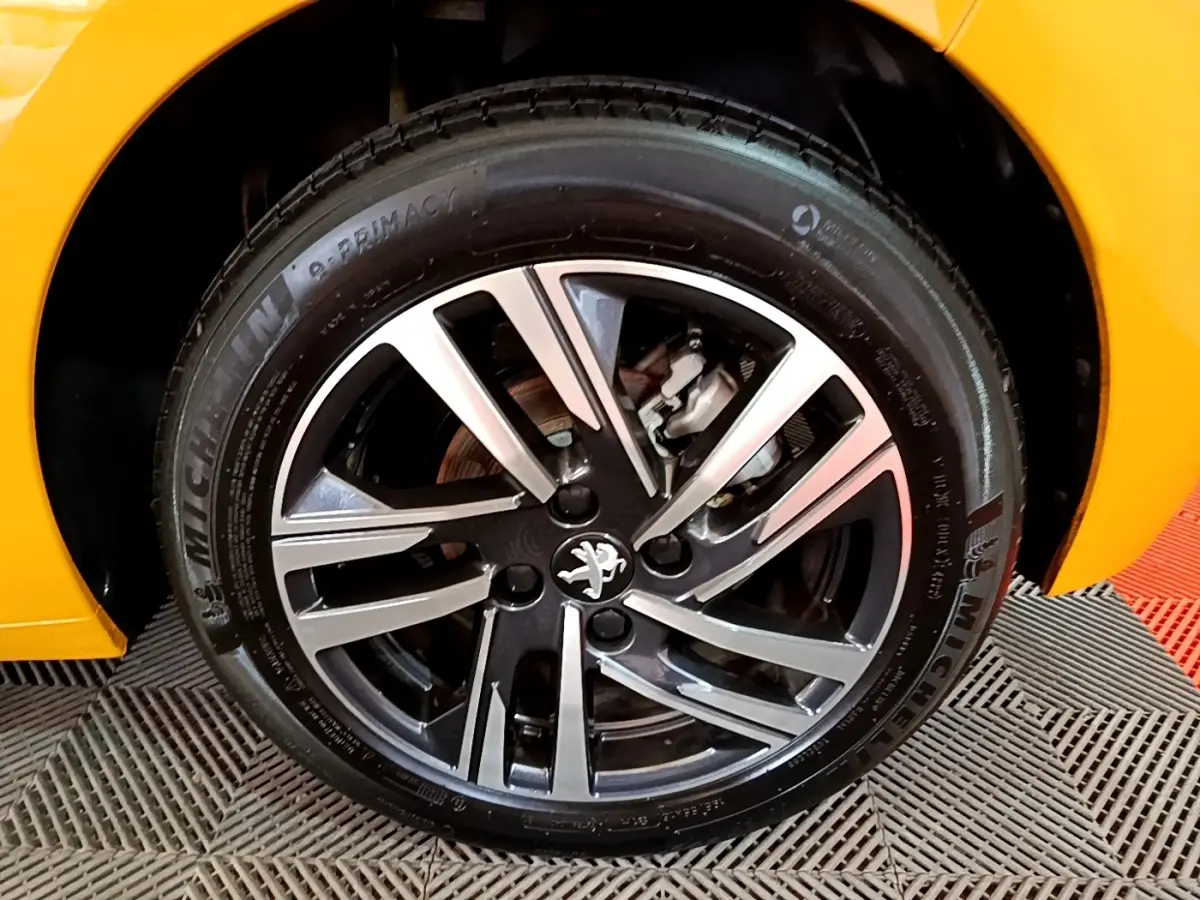 Gros plan sur la roue avant droite d’une Peugeot 208 jaune, mettant en valeur la jante alliage et le logo lion.
