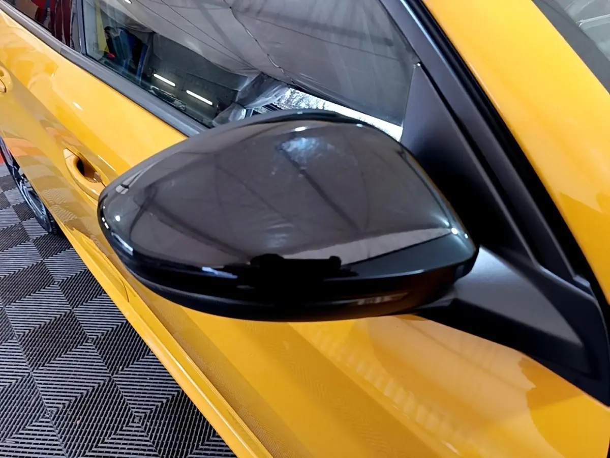 Rétroviseur noir côté gauche d’une Peugeot 208 jaune vue en léger angle depuis l’avant.