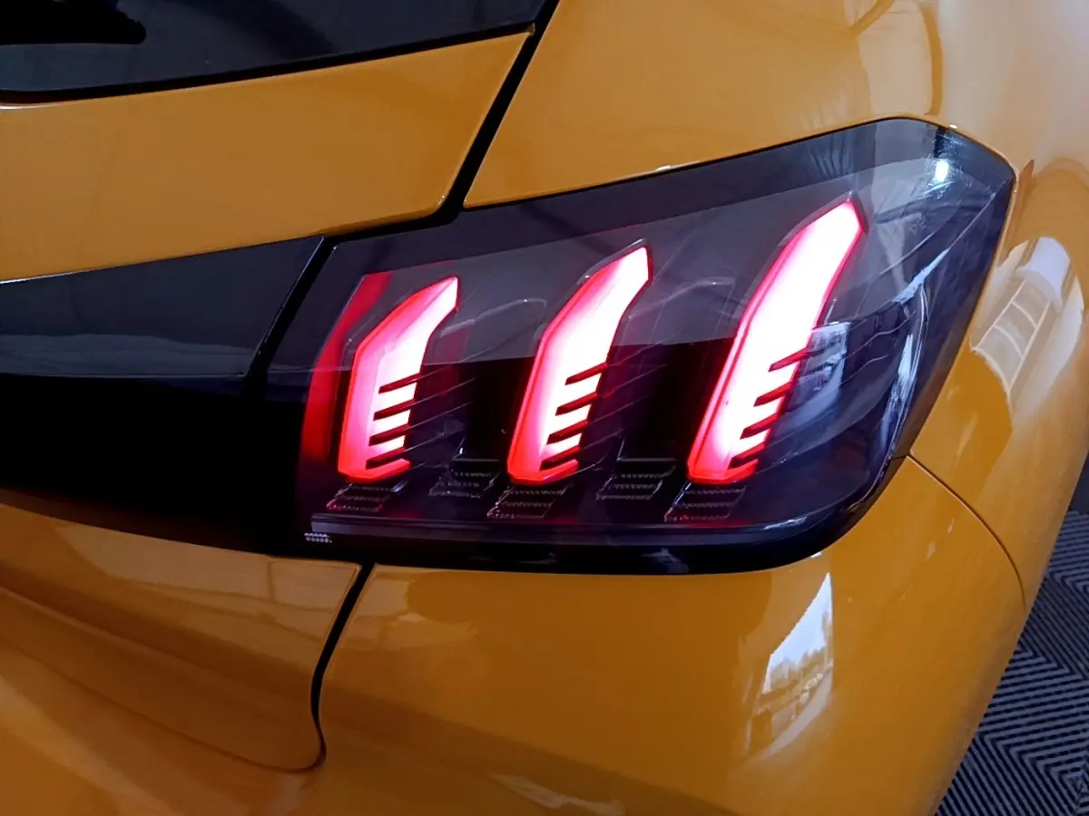 Gros plan sur le feu arrière droit allumé d’une Peugeot 208 jaune PureTech 2023, soulignant ses trois griffes lumineuses rouges.