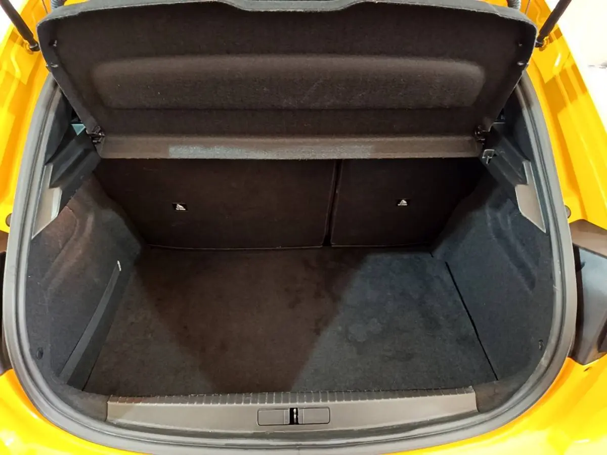 Coffre ouvert vu de dessus d'une Peugeot 208 jaune 2023, montrant un espace de rangement propre et spacieux.