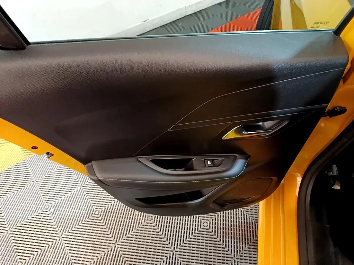 Vue rapprochée de la porte arrière gauche jaune d’une Peugeot 208 2023, avec poignée intérieure et commande de vitre noire.